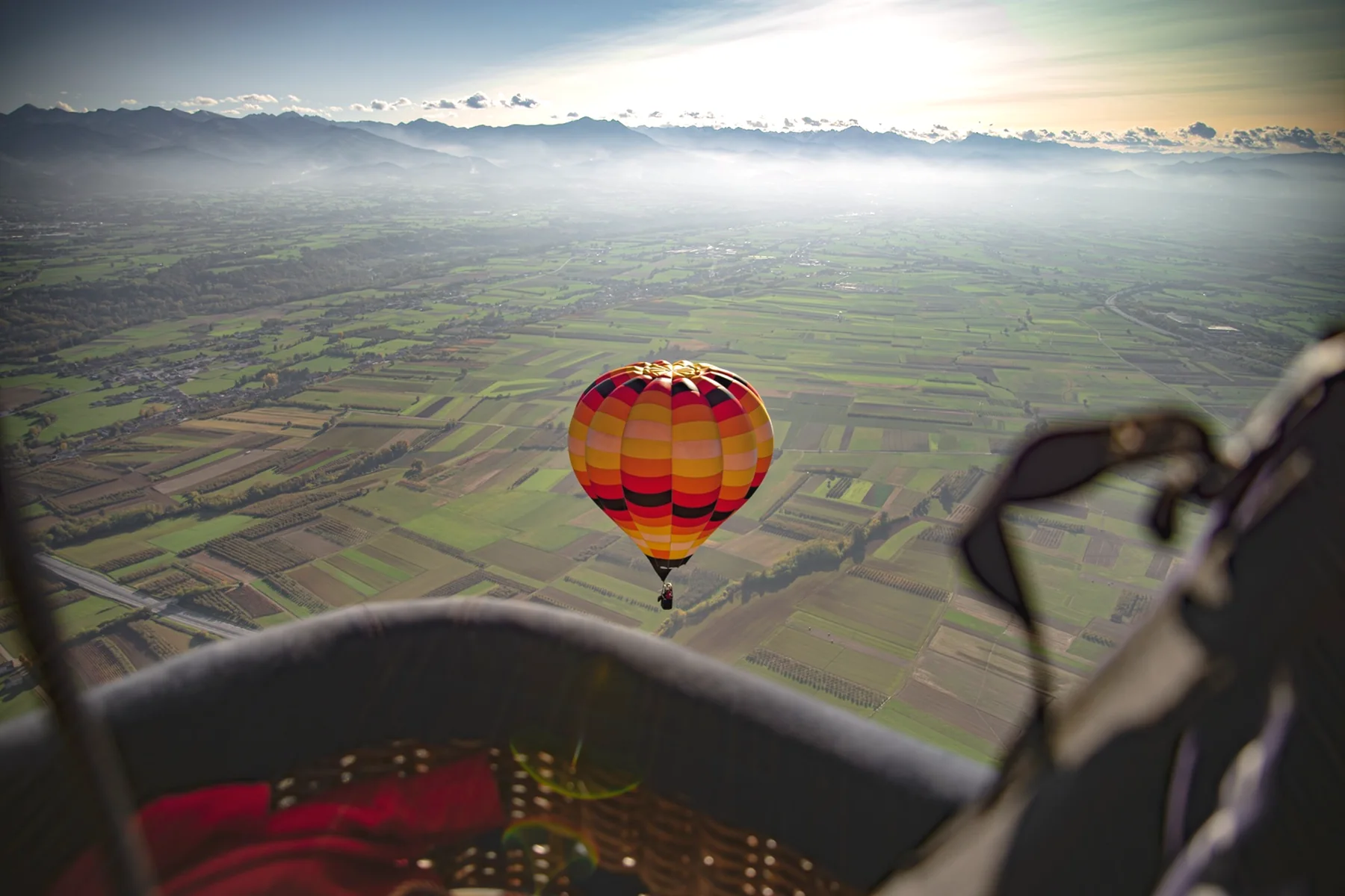 A colourful balloon seen from another basket above vineyard hills