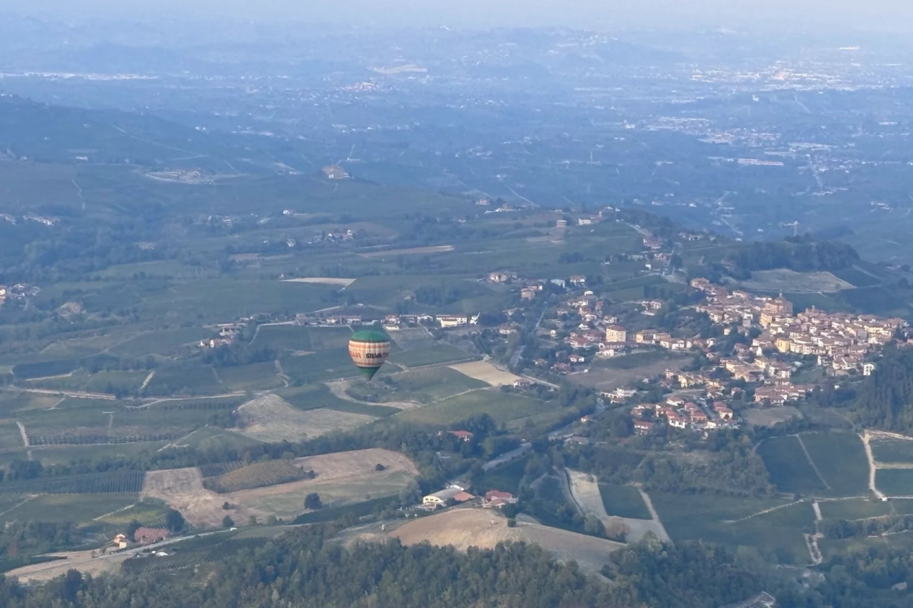 Balão sobre colinas e um vilarejo no alto da paisagem